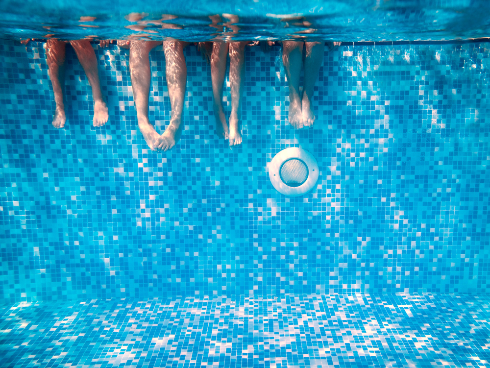 Underwater picture of kids sitting by the pool with their feet in the water | Opening your pool | Taylor Farms Water Hauling